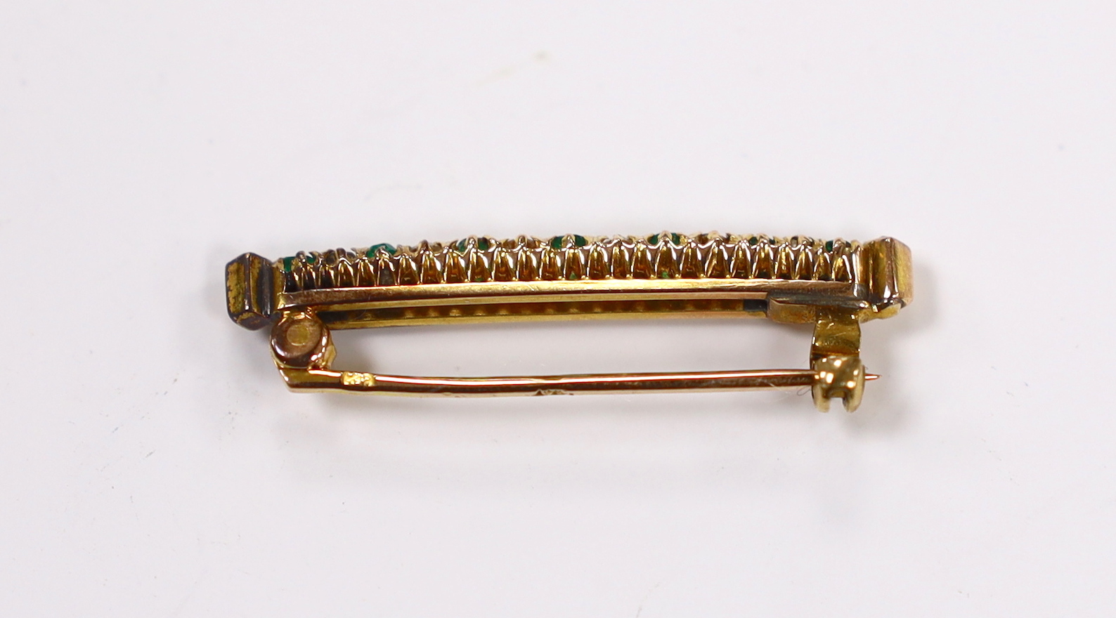 A yellow metal, seven stone emerald and eight stone diamond chip set bar brooch, 32mm, gross weight 2.9 grams.